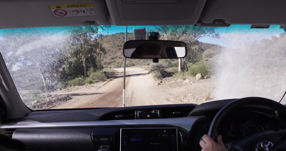 A man drives through a puddle on a dirt trail and sends water splashing onto the windshield