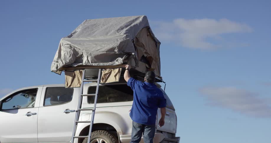 A man adjusts a tent on the back of his vehicle