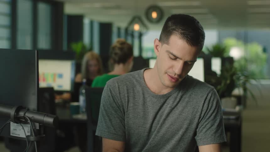 A man sitting at a desk in front of a computer writing on a notepad with a pen