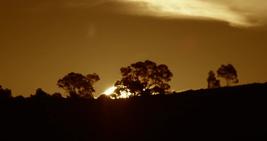 The setting sun descends behind a hill under a yellow sky