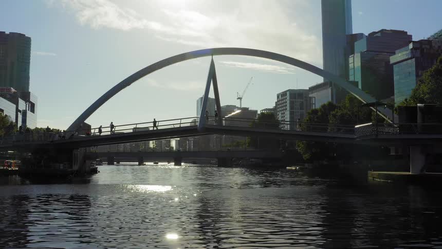 People walk on a pedestrian bridge over a river in a downtown city