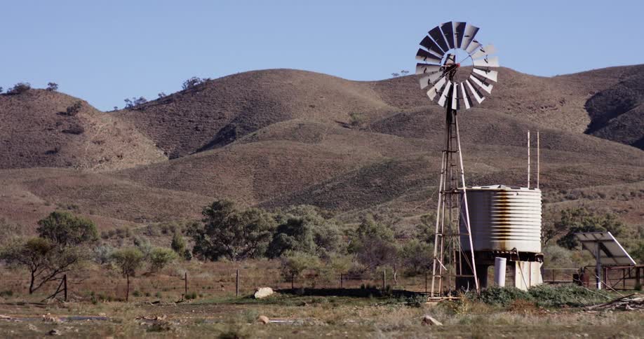 Rural area with windmill and an old silo with hills behind it on a clear day