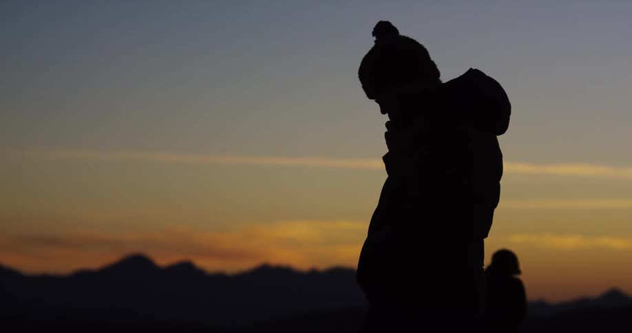 A man stands outside and looks down as the sun sets