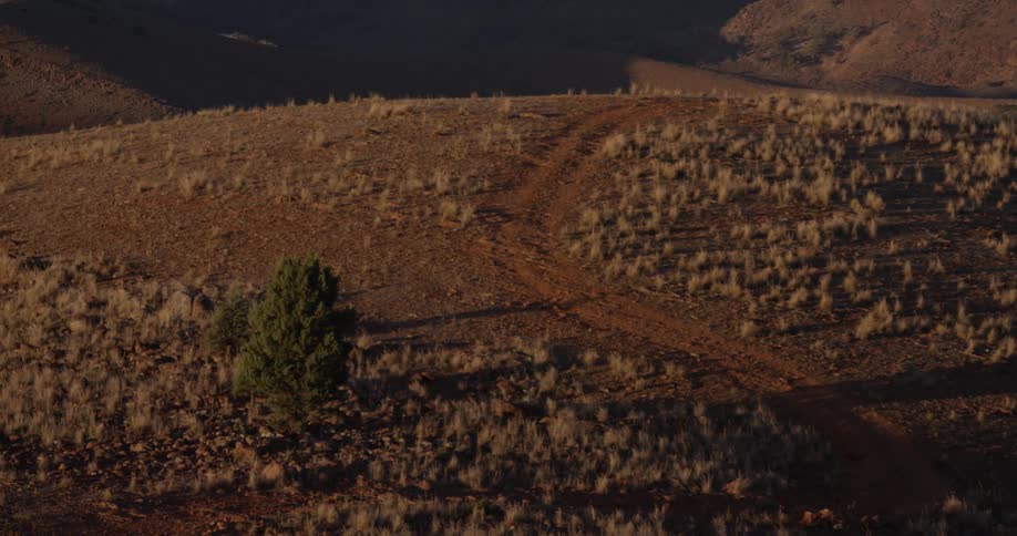 A dirt road along the top of a hill covered in sparse brown vegetation during the day