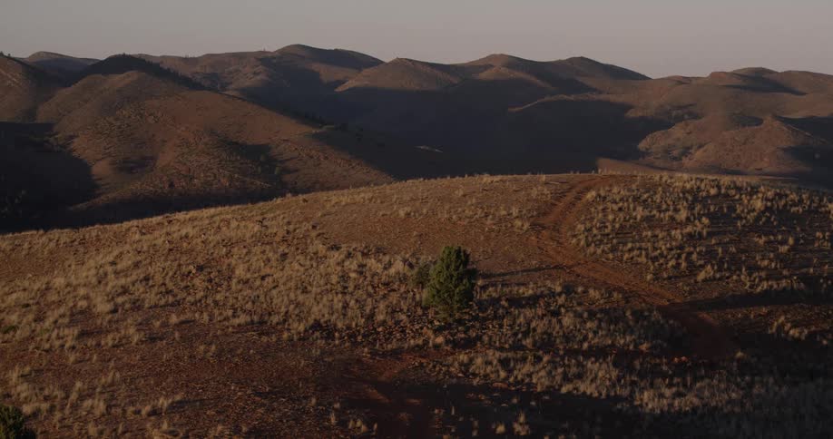 A landscape with a dirt road and a tree with hills the sky and clouds in the background