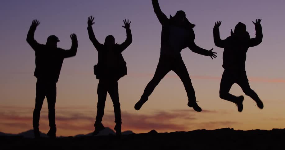 A silhouette of four people jumping with the sky and clouds in the background