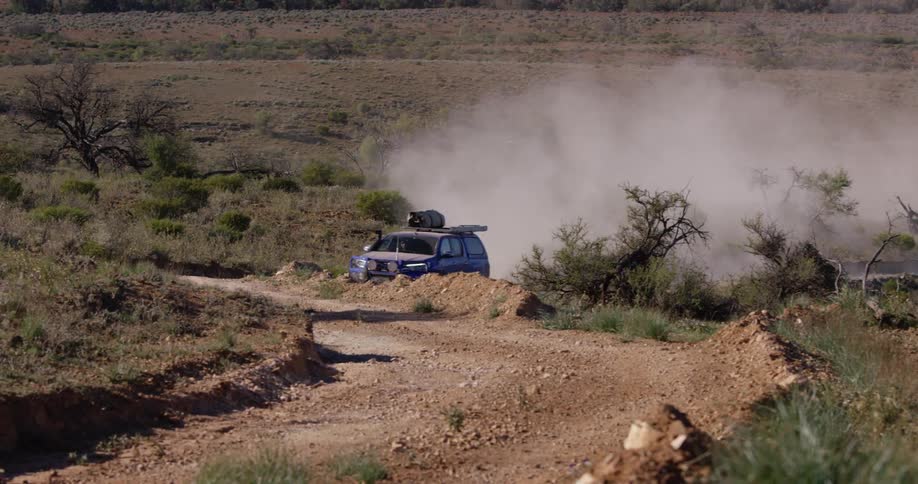 An suv with a roof rack leaves a dust trail as it travels on a desert dirt road