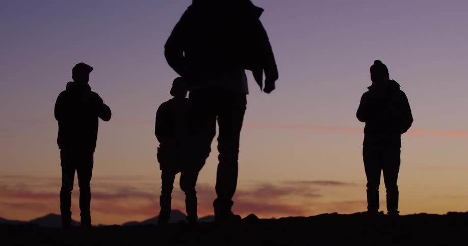 A silhouette of four people with one running with the sky and clouds in the background