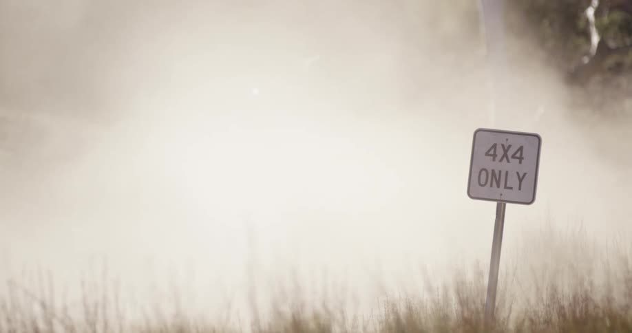 A vehicle driving on grass and smoking with a sign in the foreground and trees in the background