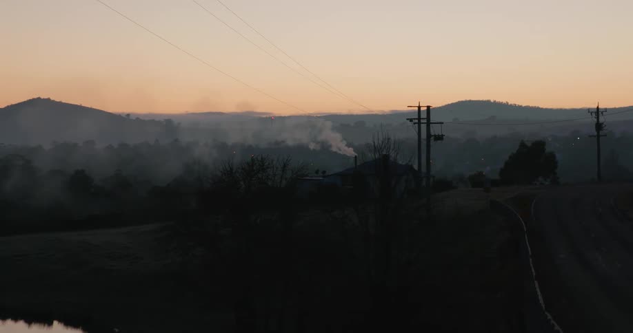 Utility poles with power lines and mountains on the horizon and smoke in the sky
