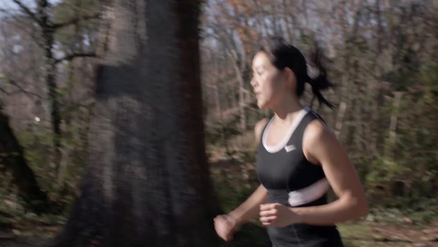 A woman is jogging on the side of a large forest