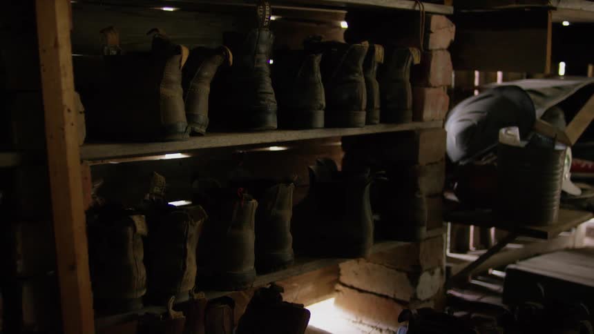 Pairs of old leather boots rest on a old shelves in a building during the day