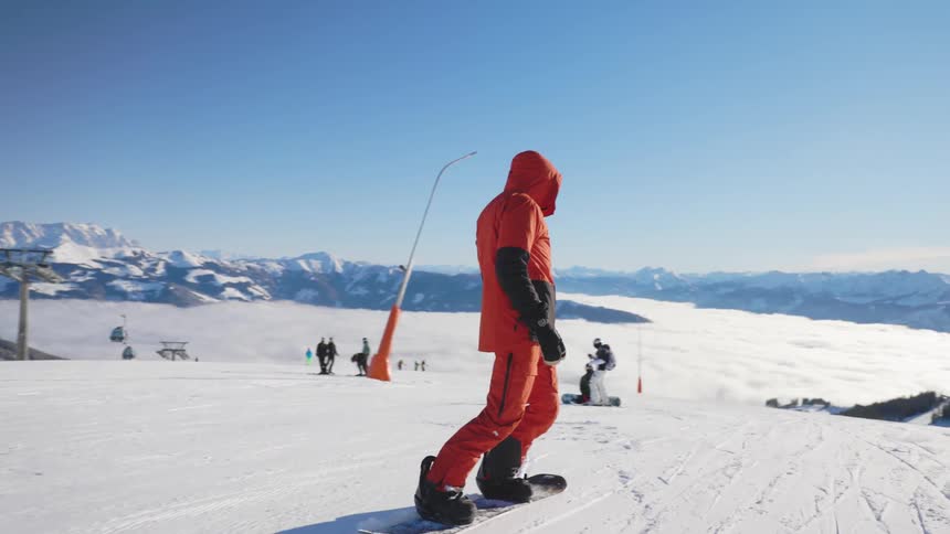 A man with gloves and a coat on a snowboard with a mountain range the sky and clouds in the background