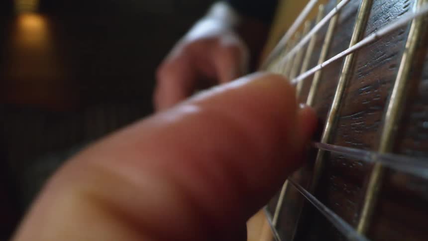 Fingers move along the strings on the neck of a musical instrument as a man plays