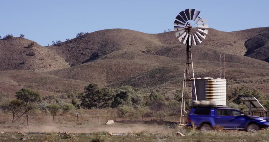 A blue sport utility vehicle drives past rolling hills and a grain silo