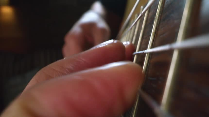 Person is playing a guitar and moving their fingers on the frets as the strum the strings