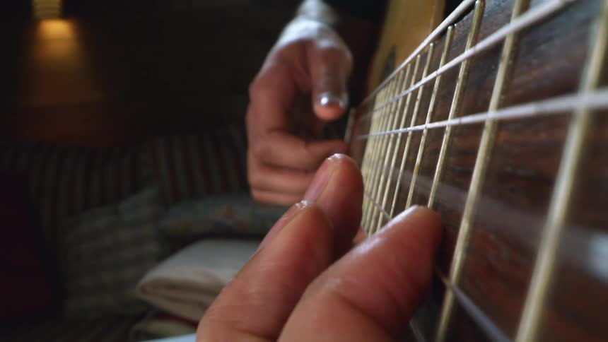 Two people picking at guitar strings in a home
