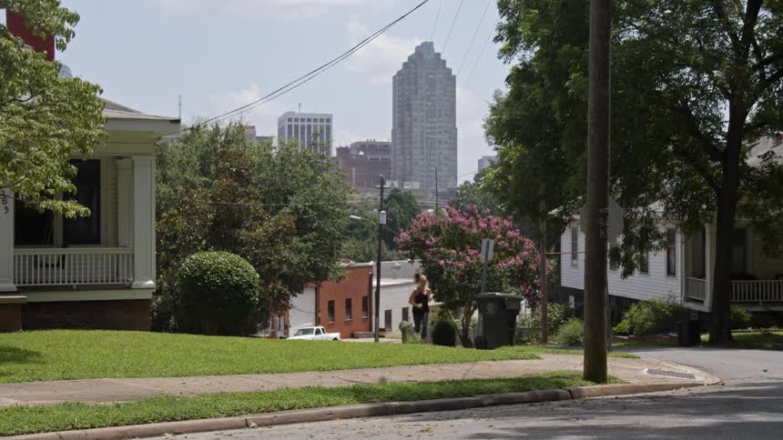A woman jogs up a hill in a suburb with a city in the background