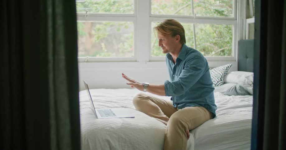 A man blows kisses at the screen of his laptop during a video call