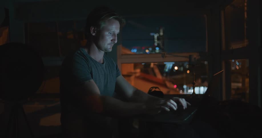 A man is typing on his laptop in the dark room