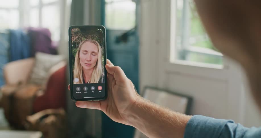 A man video chatting on a smart phone with a window and a door in the background