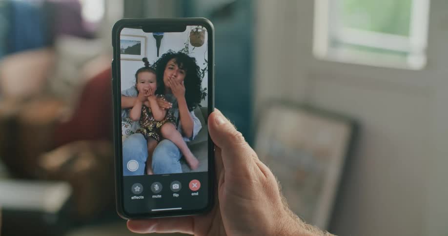 Father video calling his daughter and wife on his smartphone while they send kisses and wave