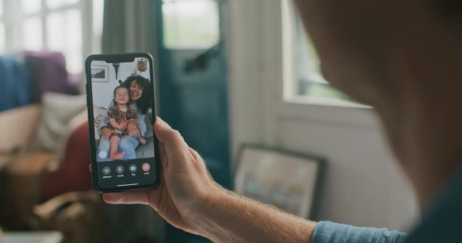 A man in a room video chatting on a smart phone with windows and a door in the background