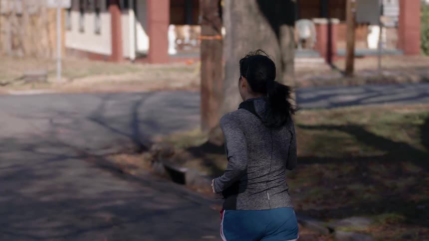 A woman is jogging up a street on a sunny day