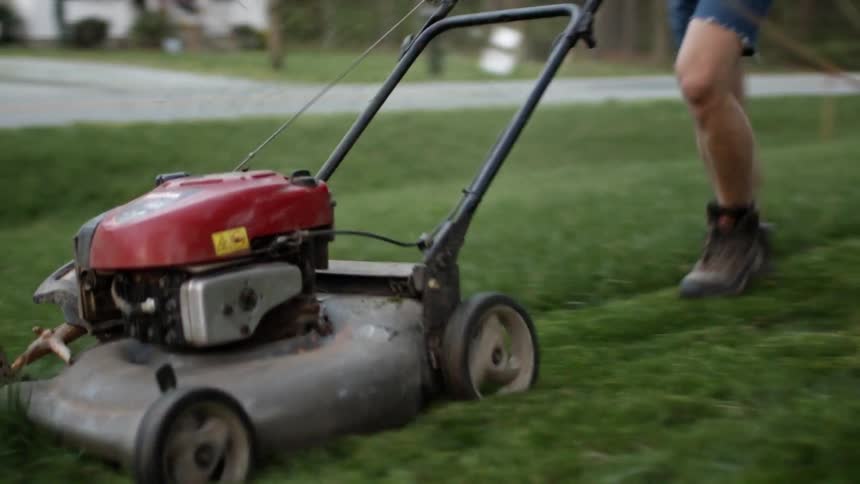 A person pushes a lawn mower across a yard