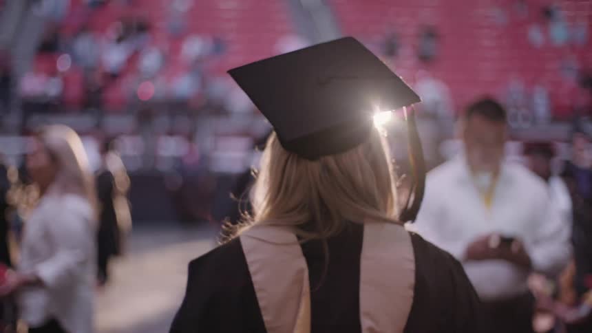 Blonde student walking among a crowd wearing her cap and gown