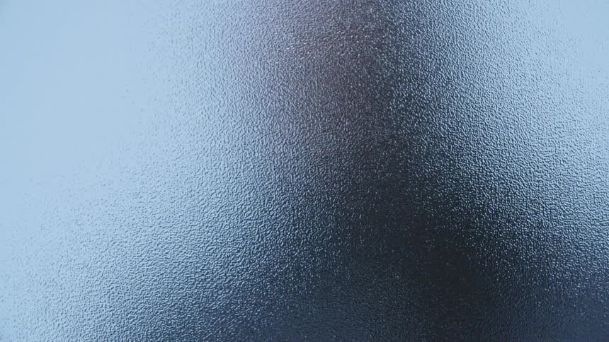 A man runs his hand along a window and presses his face to the frosted glass