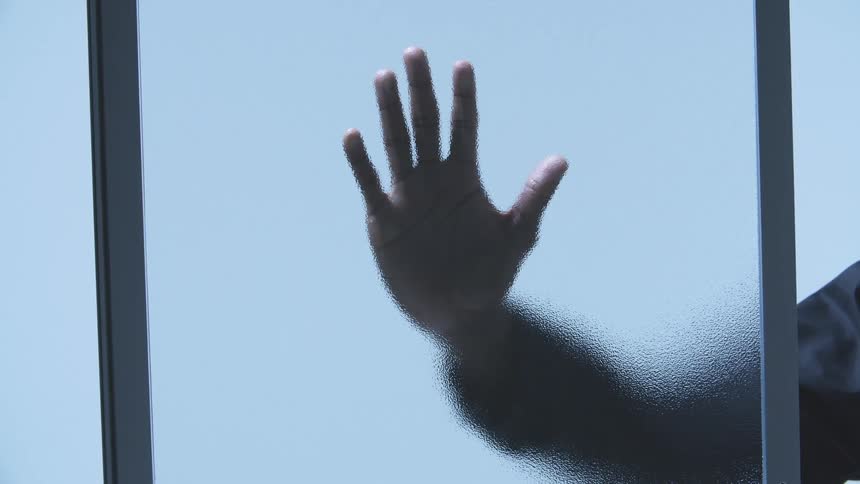 A man slaps his hand against a window pane of frosted glass