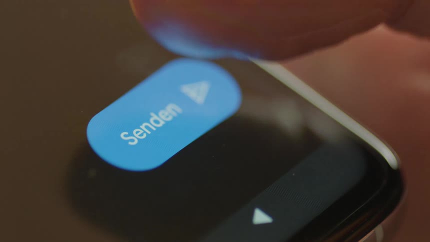 Macro close-up of a smartphone screen as a finger taps the blue “Send” button in a messaging app indoors. Filmed in soft natural light, perfect for communication, social media, UX/UI, technology, and digital interaction projects.