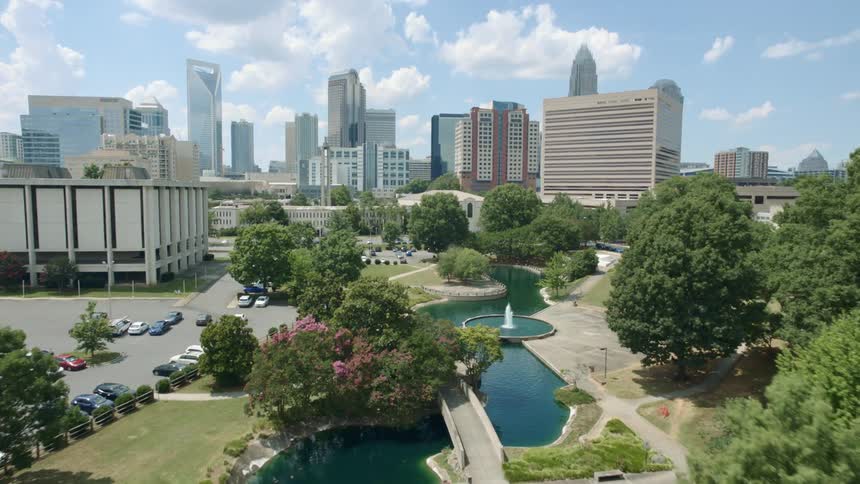An aerial view of a river flowing through an urban park with skyscrapers in the distance