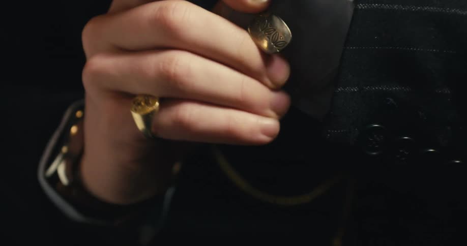 A man in a suit fastens his sleeves with a cuff link