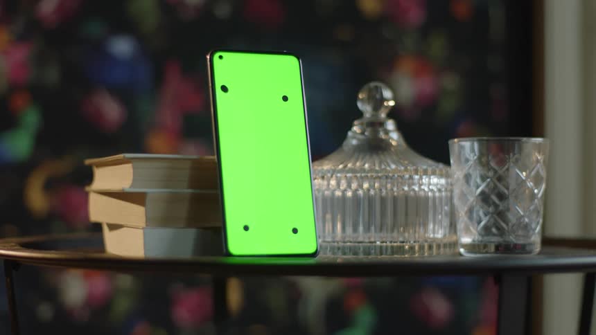 Cinematic Circular Tracking Shot Around Smartphone with Green Screen and Tracking Marks on Table with Glassware and Books. Indoor Scene for VFX and App Mockups.