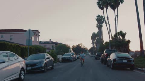 A woman rides her bicycle down the middle of a neighborhood street lined with parked cars