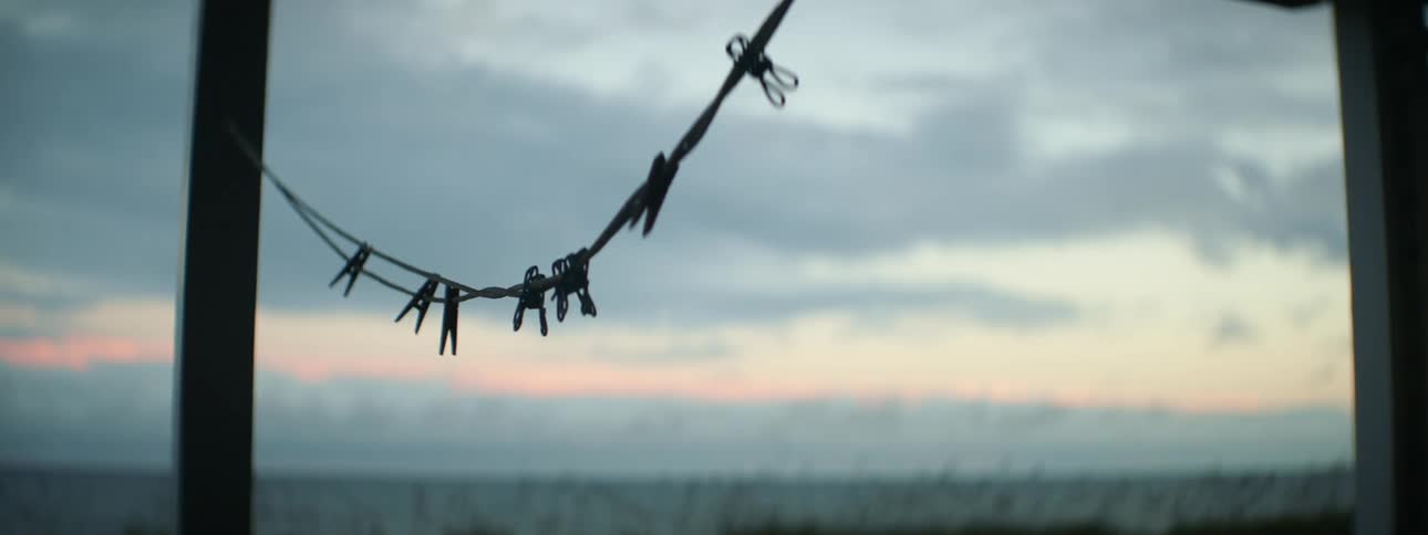 Clothes pins hang from a clothes line connected to two poles on the beach