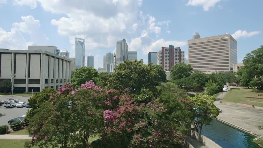 An aerial view of a pond in a city park with skyscrapers in the distance