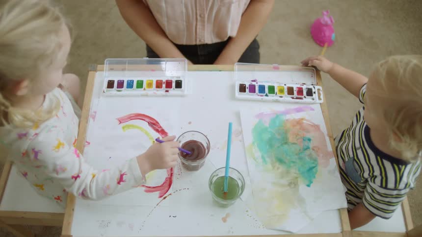 A young girl and boy using watercolors while sitting at a play table