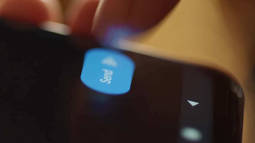 Cinematic macro close-up of a finger pressing the blue send icon on a smartphone touchscreen. Captured indoors in warm natural light, perfect for illustrating texting, social communication, UX/UI interaction, and modern digital interfaces.