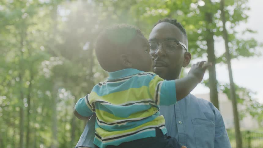 A man holding a small boy while standing outdoors kisses the boy on the forehead