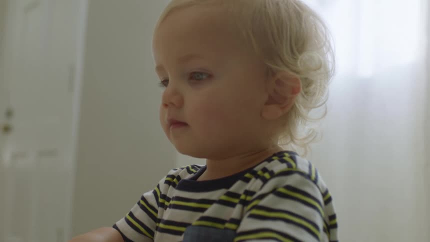 A blonde toddler in a room with sunlight coming through sheer drapes