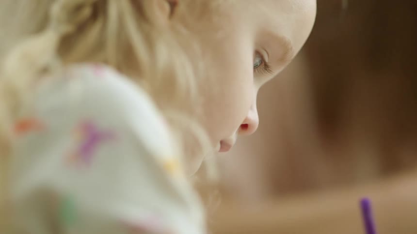 A child is drawing with a purple crayon