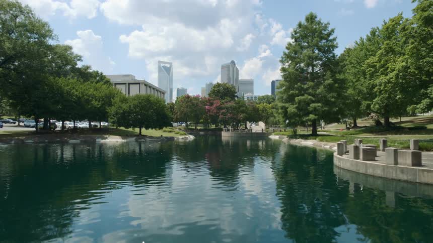 Sky and clouds are reflected on the surface of the shimmering water in a city park with skyline behind
