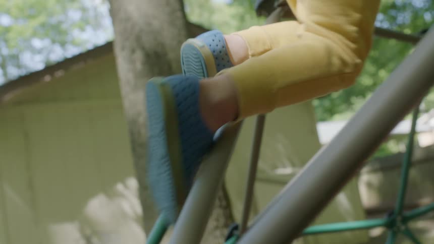 A child climbing a jungle gym with houses trees the sky and clouds in the background
