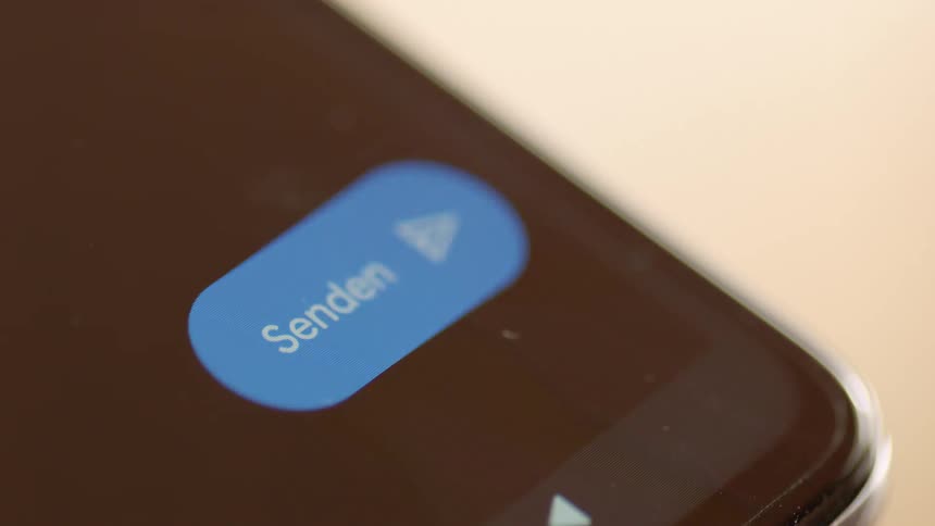 Macro close-up of smartphone screen as finger taps blue “Send” button in messaging app. Filmed in soft natural light, perfect for communication, social media, UX/UI, and technology projects focusing on digital interaction and mobile apps.