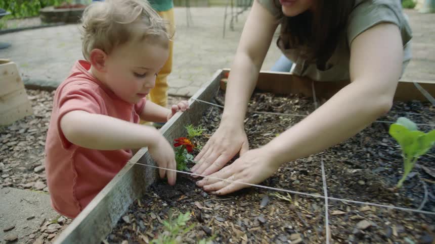 A mother plants flowers outside her home with her two sons