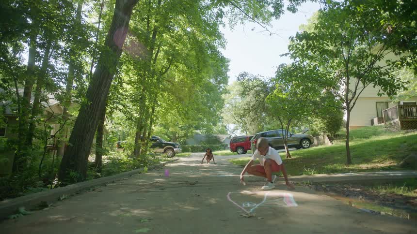A brother and sister draw in chalk on the street in front of their home