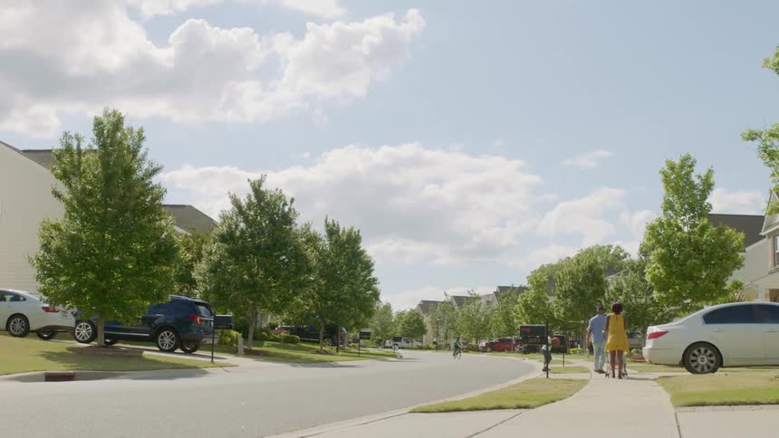 A family walks down a sidewalk through a residential neighborhood on a sunny day